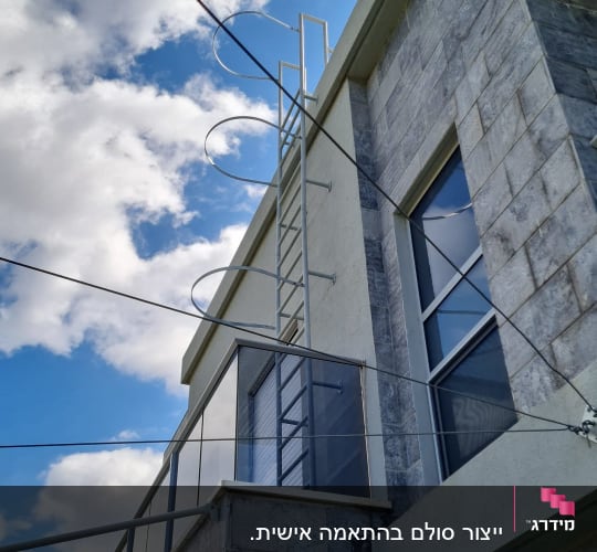 סולם מתכת חיצוני עם כלוב הגנה מותקן על קיר בית לעלייה לגג